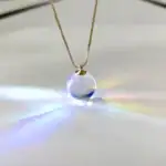 Collier avec pendentif boule en verre transparent, capturant la lumière pour créer un effet lumineux et coloré. Parfait pour les amateurs de décoration scientifique et d'objets uniques.