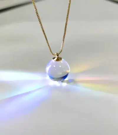 Collier avec pendentif boule en verre transparent, capturant la lumière pour créer un effet lumineux et coloré. Parfait pour les amateurs de décoration scientifique et d'objets uniques.