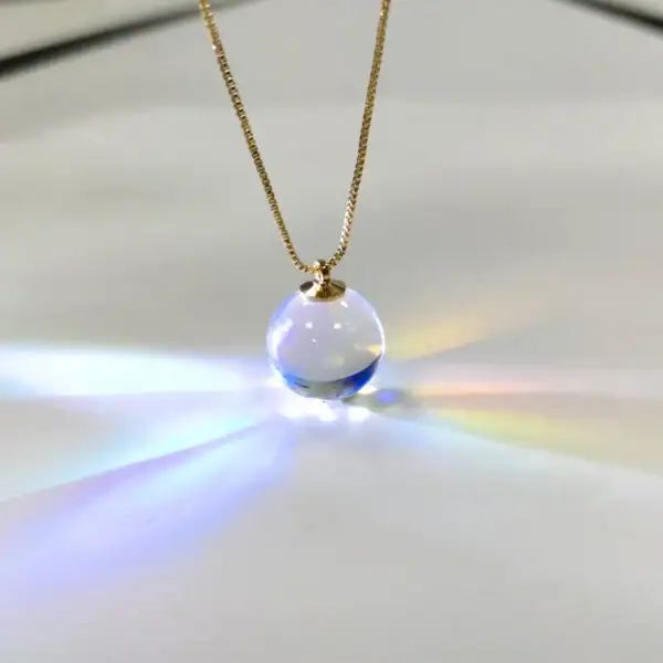 Collier avec pendentif boule en verre transparent, capturant la lumière pour créer un effet lumineux et coloré. Parfait pour les amateurs de décoration scientifique et d'objets uniques.