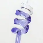 Pendentif en verre violet en forme de spirale, suspendu par un fil transparent, mettant en valeur sa transparence et ses reflets lumineux.