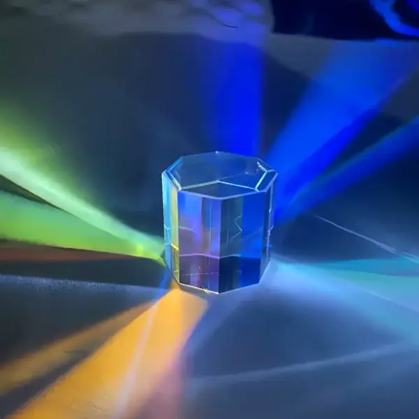 Pendentif en cristal hexagonal transparent avec effets lumineux colorés, projetant des reflets multicolores sur la surface environnante.
