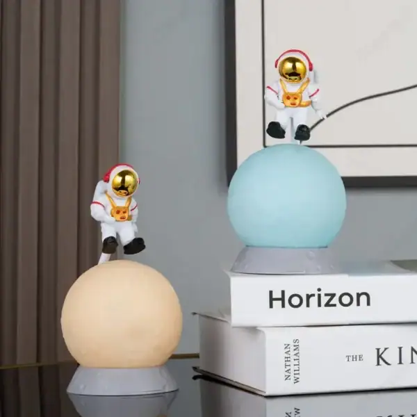Deux figurines d'astronautes en plastique avec casques dorés, posées sur des sphères lumineuses, décorant un intérieur moderne avec des livres en arrière-plan.