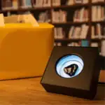 Petite boîte à illusions optiques avec un motif circulaire lumineux, posée sur une table en bois dans une bibliothèque.