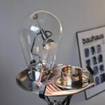 Lampe décorative en forme d'ampoule avec filament visible, posée sur un plateau avec une tasse en métal.