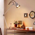 Lampe de bureau industrielle vintage avec bras articulé en métal, éclairant un bureau avec des objets de décoration scientifique et vintage.