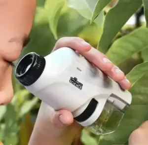 Enfant utilisant un microscope portatif pour explorer la nature, avec des feuilles vertes en arrière-plan, idéal pour l'apprentissage scientifique ludique.
