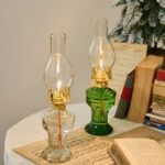 Deux anciennes lampes à huile en verre et laiton, décoratives, posées sur une table avec livres et une petite sapin de Noël en arrière-plan.