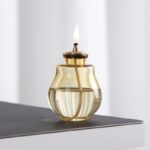 Lampe à huile décorative en verre avec mèche et flamme allumée.