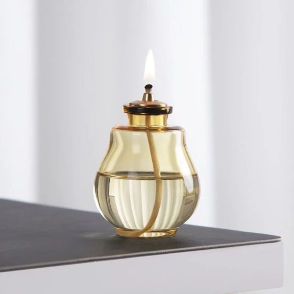 Lampe à huile décorative en verre avec mèche et flamme allumée.