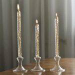 Trois bougeoirs en verre transparent avec bougies allumées, élégants et modernes, placés sur une table en bois, créant une ambiance chaleureuse.