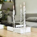 Trois bougeoirs en verre avec bougies allumées, posés sur une table en bois, décoration élégante et moderne pour intérieur.