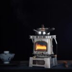 Pistolet Ă gaz vintage en mĂ©tal, utilisĂ© pour le camping et la randonnĂ©e, avec une flamme allumĂ©e visible Ă travers la fenĂȘtre de la chaudiĂšre.