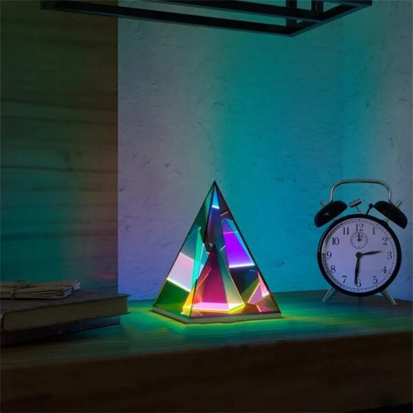 Lampe scientifique en forme de pyramide avec éclairage coloré, accompagnée d'une horloge réveil vintage sur un bureau en bois.