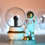 Vitrine avec figurine d'astronaute en tenue spatiale, posée à côté d'un globe de verre, évoquant l'exploration spatiale et la science.