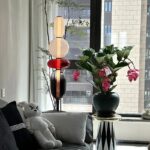 Vase de fleurs avec décoration scientifique moderne, comprenant un arrangement floral avec des feuilles vertes et des fleurs roses, placé près d'une fenêtre dans un intérieur contemporain.