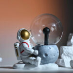 Figurine d'astronaute en décoration de science, assise à côté d'une ampoule à filament dans un décor minimaliste.