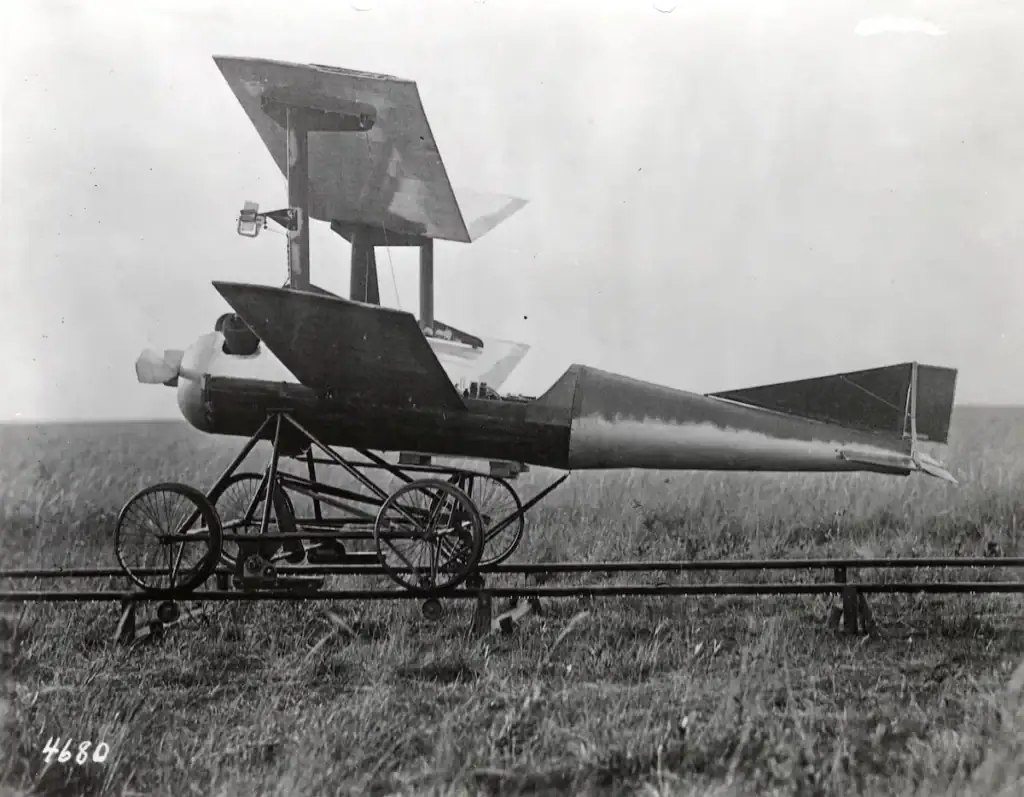 Historische Rakete auf einer Wiese, vermutlich ein frühes Raumfahrtmodell, mit großen Flügeln und einem langen Rumpf, auf einem fahrbaren Gestell montiert.