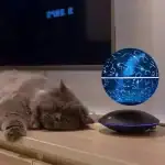 Globe terrestre représentant une carte stellaire et constellations, posé sur une surface en bois, avec un chat endormi à côté.