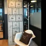 Panneau décoratif représentant le tableau périodique des éléments chimiques avec un fauteuil moderne et un coussin scientifique, idéal pour une décoration de style scientifique ou éducatif.