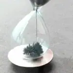 Horloge de sable en verre avec sable noir, symbole de temps et de science, utilisée comme décoration ou objet scientifique.