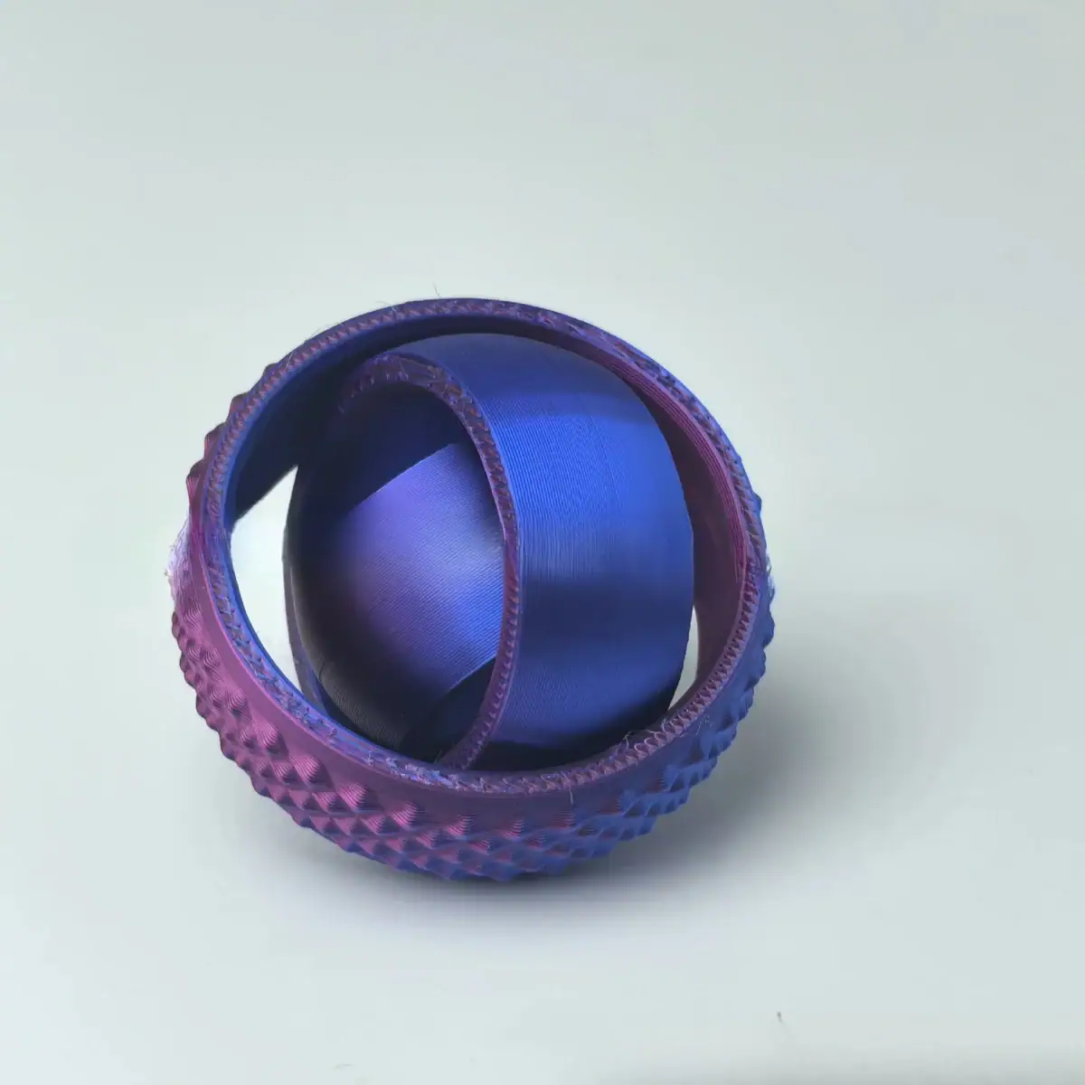 Balle de tennis en métal peint en violet avec surface texturée, utilisée comme objet décoratif ou scientifique.