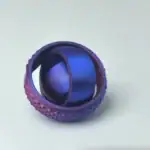 Balle de tennis en métal peint en violet avec surface texturée, utilisée comme objet décoratif ou scientifique.