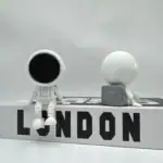 Figurines d'explorateurs scientifiques en style minimaliste avec casque et globe, sur une plateforme avec le mot "LONDON" en lettres noires.