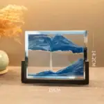Panneau en verre avec paysage de montagnes bleues, encadré et posé sur une surface en bois.