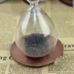 Sablier en verre contenant une mousse de carbone noire, posé sur une surface en papier avec texte scientifique.