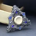 Fidget spinner décoratif en métal avec détails en bleu et design complexe, idéal pour la décoration ou la collection.