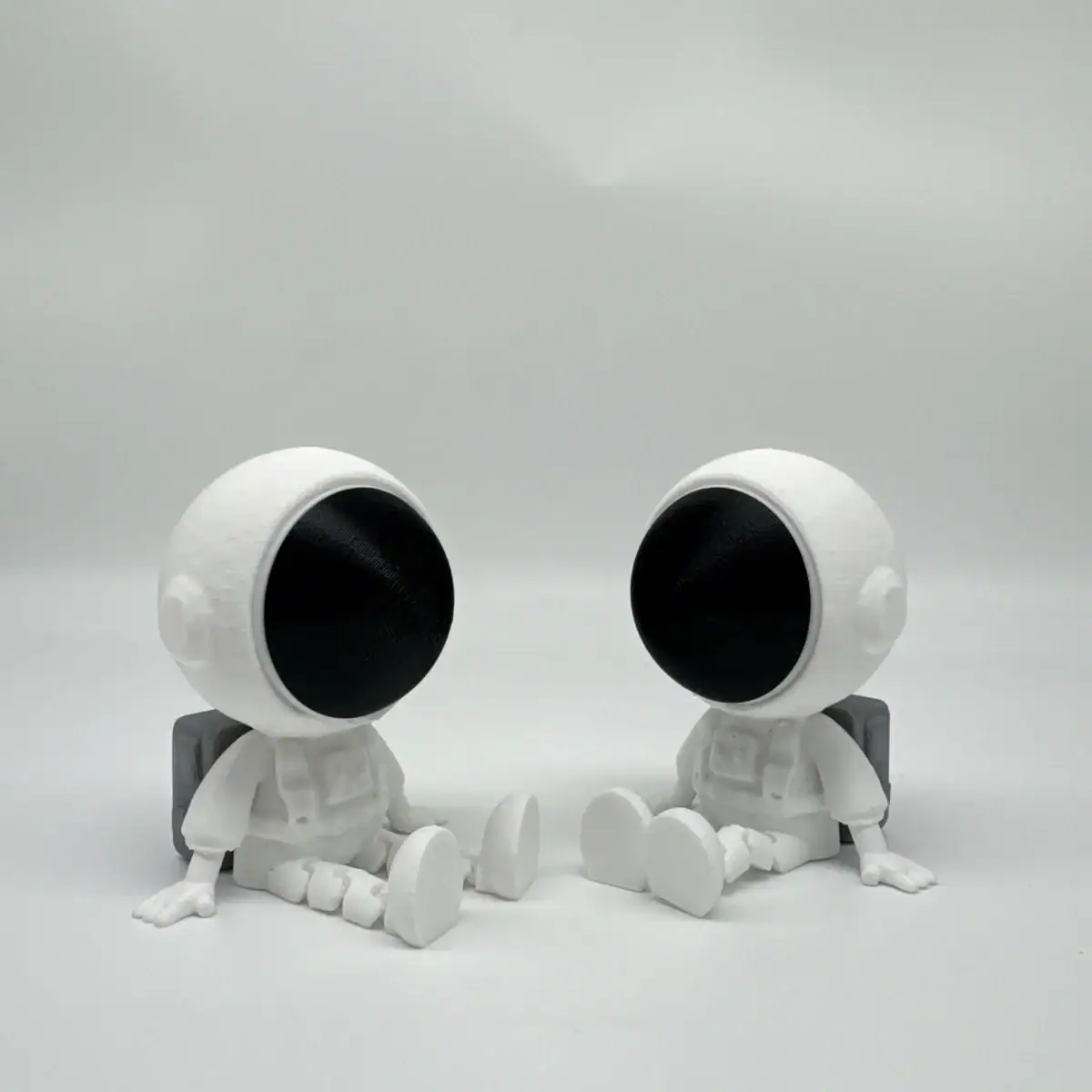 Deux figurines d'astronautes en plastique blanc avec des visages noirs, assises sur un fond blanc, décor de style scientifique et ludique.