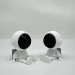 Deux figurines d'astronautes en plastique blanc avec des visages noirs, assises sur un fond blanc, décor de style scientifique et ludique.
