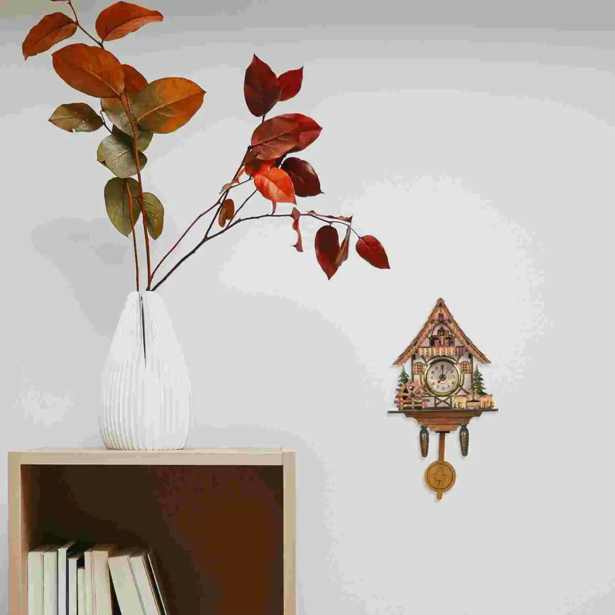 Vase blanc avec branches aux feuilles rouges et vertes, décoratif, avec horloge de style chalet en bois suspendue au mur.