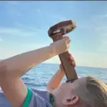 Enfant utilisant un pupitre scientifique en bois avec loupe intégrée, face à la mer, pour explorer la nature et la science en plein air.