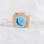 Petite caméra en bois naturel avec objectif bleu, idéale pour la décoration ou le jeu chez les enfants, apportant une touche ludique et éducative à la décoration.