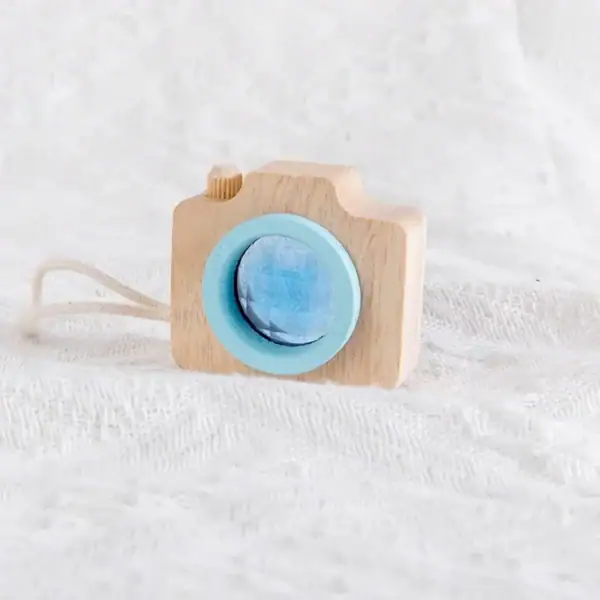 Petite caméra en bois naturel avec objectif bleu, idéale pour la décoration ou le jeu chez les enfants, apportant une touche ludique et éducative à la décoration.