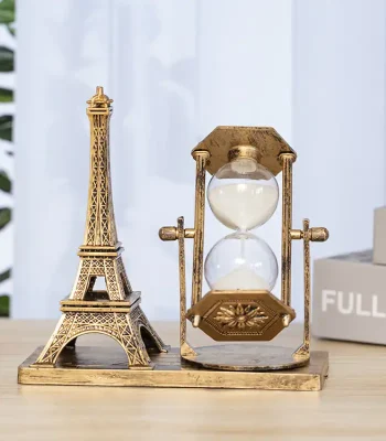 Sablier décoratif en laiton avec motif vintage, représentant un sablier classique avec un cadre en laiton antique, placé à côté d'une miniature de la Tour Eiffel en métal doré.