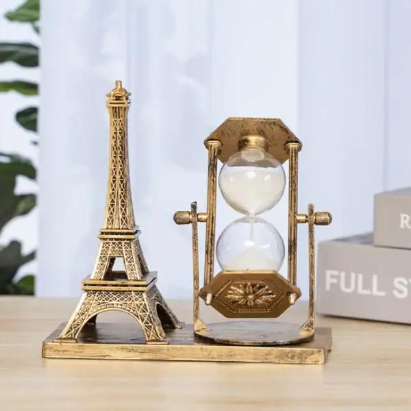 Sablier décoratif en laiton avec motif vintage, représentant un sablier classique avec un cadre en laiton antique, placé à côté d'une miniature de la Tour Eiffel en métal doré.