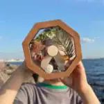 Pendentif en bois avec éléments naturels, comme des feuilles et des pierres, présenté devant un paysage marin. Idéal pour la décoration ou comme accessoire original inspiré de la science.