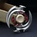 Fidget spinner en métal avec design complexe, pièces mécaniques et détails rouges, posé sur une surface sombre.