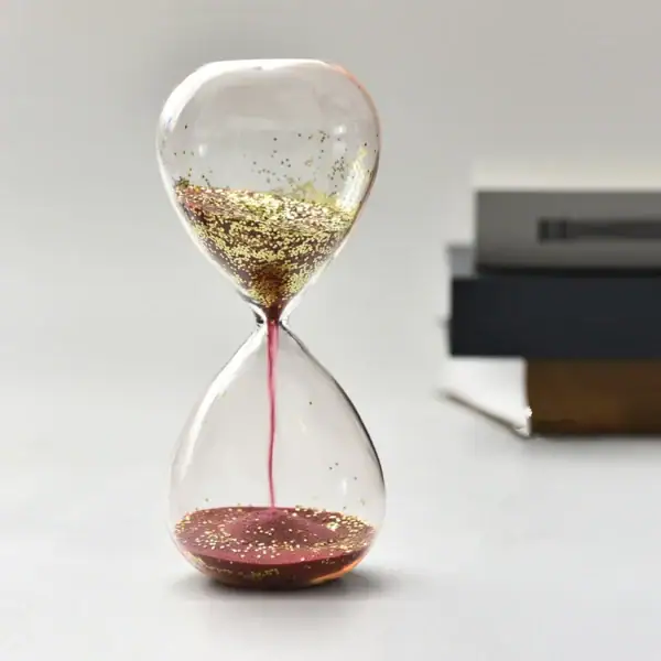 Balancier de sablier avec liquide doré et rose, symbole de la science et du temps.