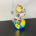 Figurine LEGO d'astronaute avec casque doré, assise sur une planète colorée, représentant une scène spatiale ludique et créative.