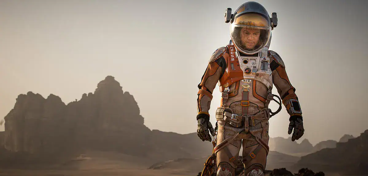 Explorateur en combinaison spatiale dans un paysage désertique avec montagnes en arrière-plan.