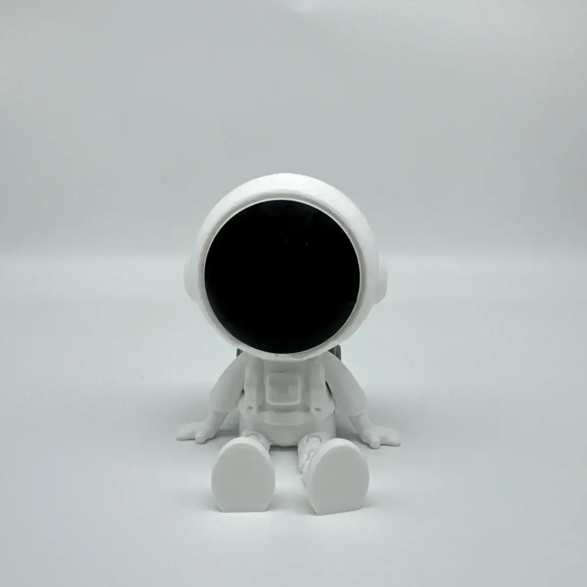 Robot miniature en plastique blanc avec un visage noir, assis sur une surface blanche, évoquant la science et la technologie.
