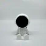 Robot miniature en plastique blanc avec un visage noir, assis sur une surface blanche, évoquant la science et la technologie.