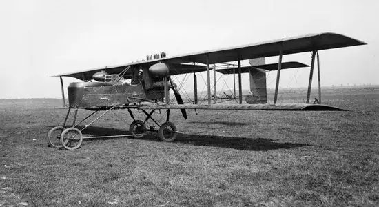 Historisches Flugzeugmodell aus den frühen Tagen der Luftfahrt, mit offener Kabine und großen Flügeln, auf einer Wiese präsentiert.