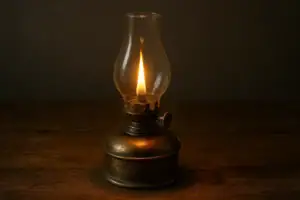 Lampe à pétrole ancienne en verre transparent et base en métal, éclairant doucement dans l'obscurité.
