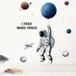 Illustration d'un astronaute tenant un ballon représentant une planète, avec d'autres corps célestes autour, accompagnée du texte "I NEED MORE SPACE" pour un décor scientifique et spatial.