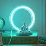 Lampe de décoration scientifique avec anneau lumineux bleuté et figurine de dinosaure sur une base lunaire.