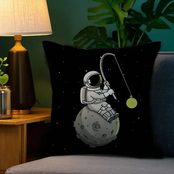 Coussin avec design d'astronaute pêchant dans l'espace, posé sur un canapé.
